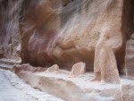 Petra,  Here in a badly weathered condition is the remains of a statue that included a Nabetean and a couple of camels.   The Nabetean is visible from the waist down in the right forground.  The camels are visible at their feet,  and the one closest to the Nabetean at his belly.  All the camels legs have eroded away.  Note the water channel carved in behind the legs of the Nabetean and the camels.